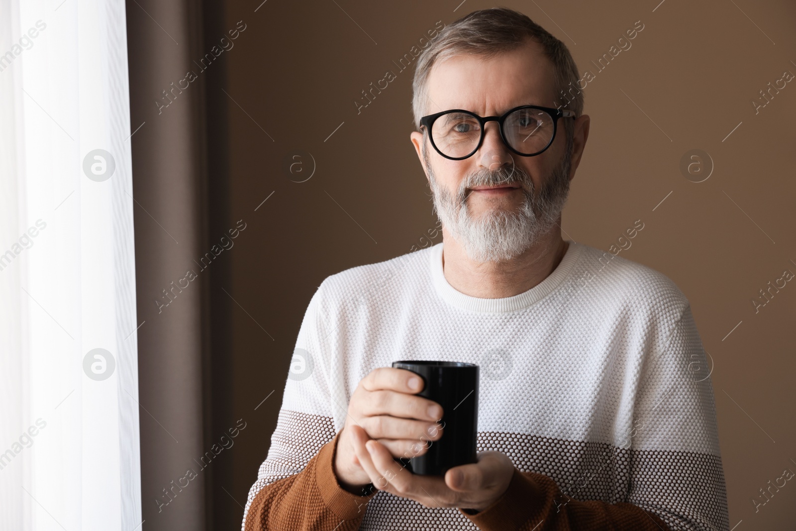 Photo of Mature man with cup of hot drink at home. Space for text