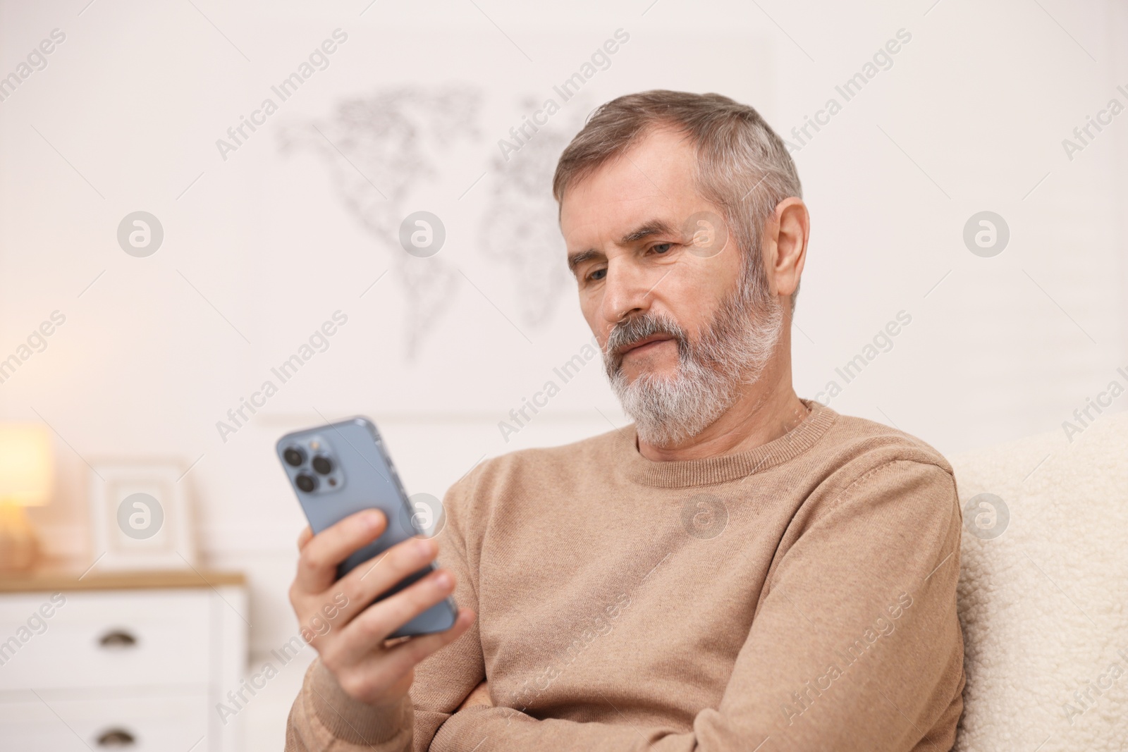 Photo of Mature man looking at smartphone at home