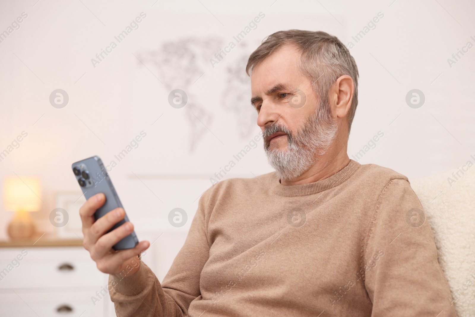 Photo of Mature man looking at smartphone at home