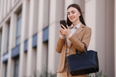 Photo of Smiling businesswoman in stylish suit using smartphone outdoors, low angle view. Space for text