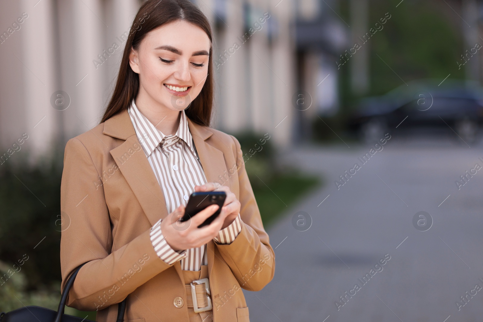 Photo of Smiling businesswoman in stylish suit using smartphone outdoors. Space for text