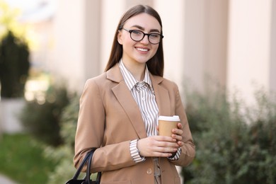 Photo of Smiling businesswoman in stylish suit with paper cup outdoors