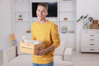 Photo of Happy man holding wooden crate with stuff in new apartment. Housewarming party