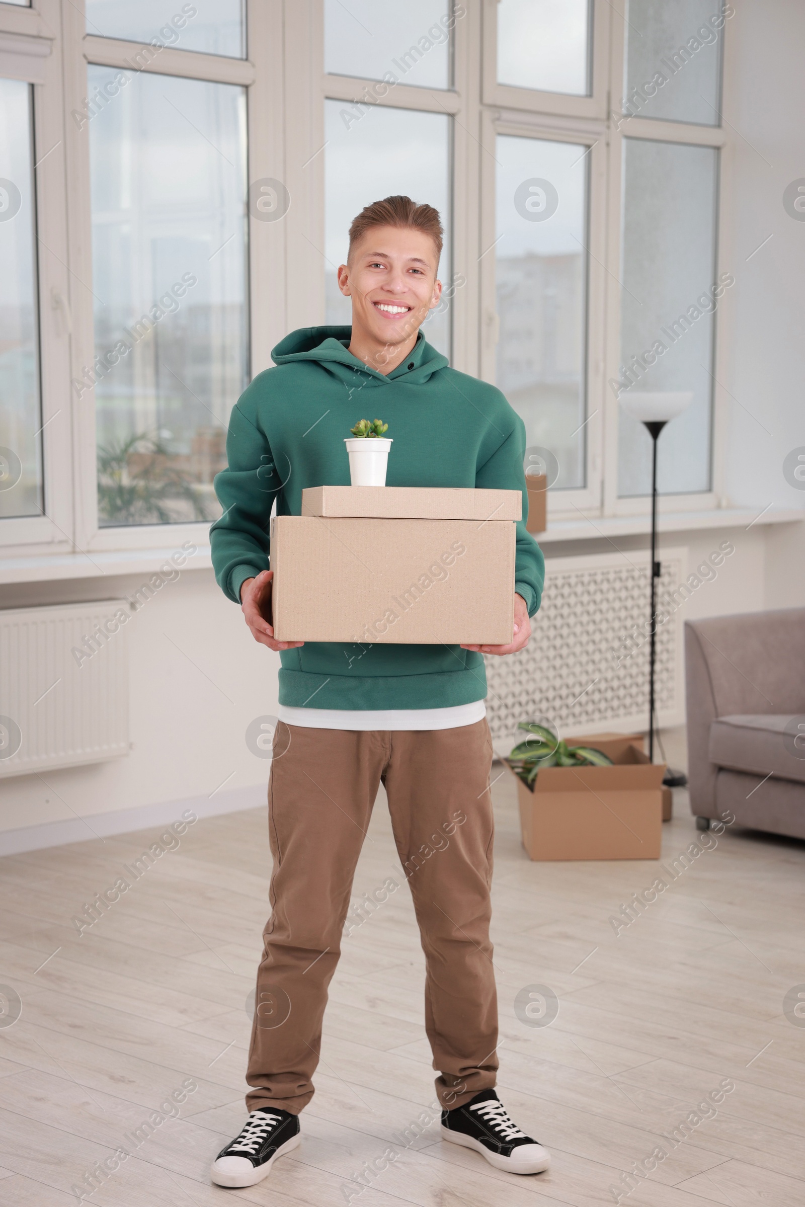 Photo of Happy man with moving boxes and houseplant in new apartment. Housewarming party