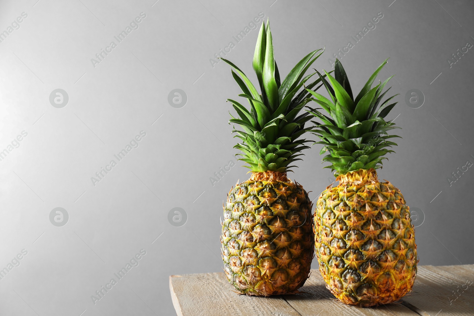 Photo of Fresh ripe pineapples on wooden table against light grey background. Space for text