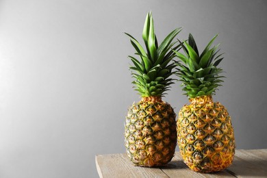 Photo of Fresh ripe pineapples on wooden table against light grey background. Space for text