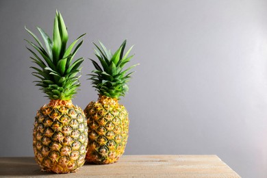 Fresh ripe pineapples on wooden table against light grey background. Space for text