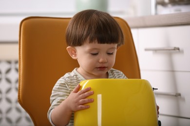 Photo of Little boy playing with toaster in kitchen. Dangerous situation