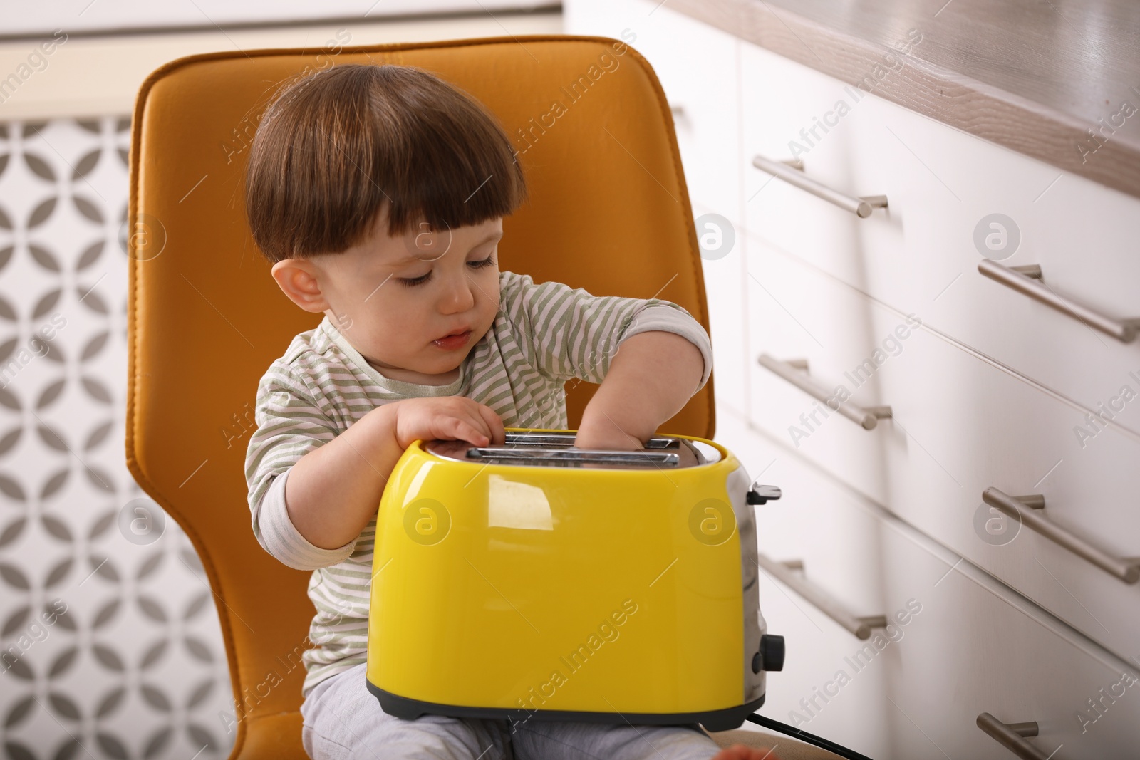 Photo of Little boy playing with toaster in kitchen. Dangerous situation