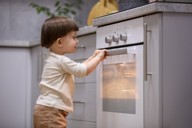 Photo of Little boy playing with oven in kitchen. Dangerous situation