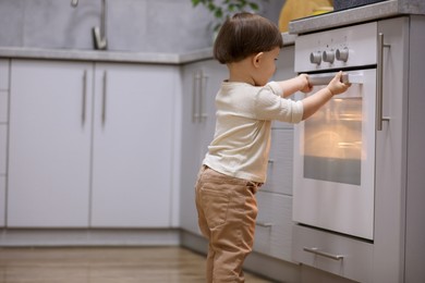 Photo of Little boy playing with oven in kitchen. Dangerous situation