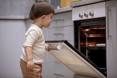 Photo of Little boy playing with oven in kitchen. Dangerous situation