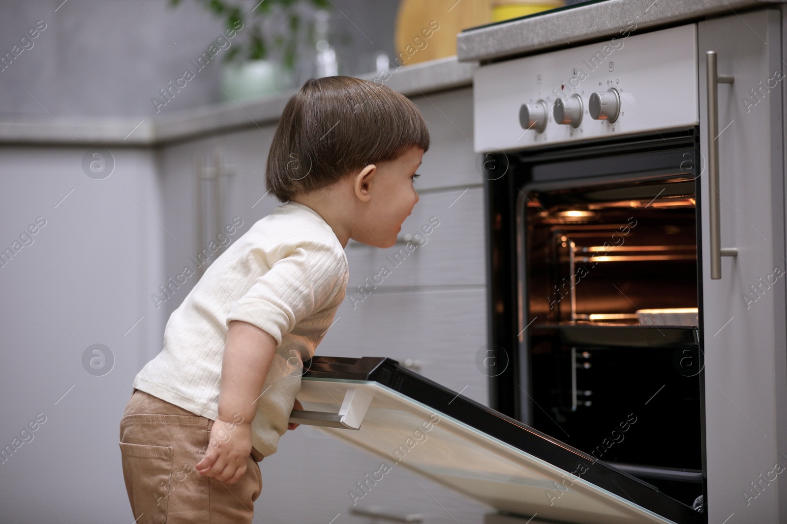 Photo of Little boy playing with oven in kitchen. Dangerous situation