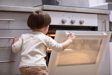 Photo of Little boy playing with oven in kitchen, back view. Dangerous situation