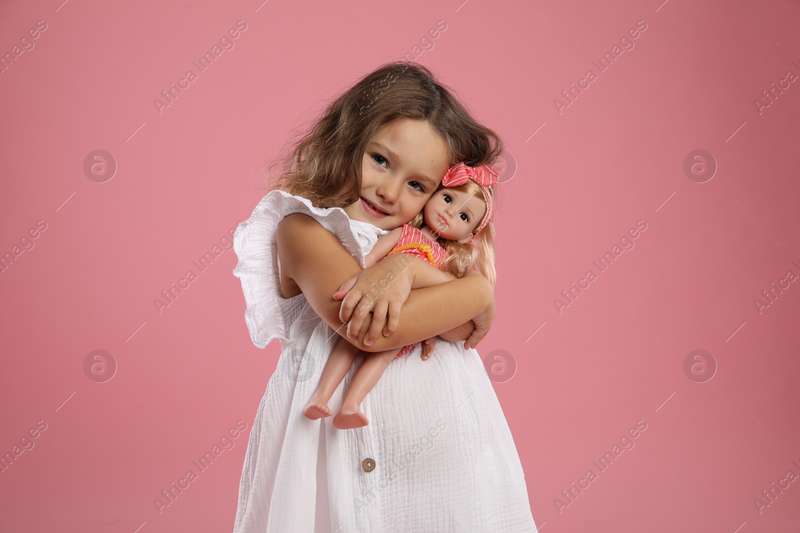 Photo of Cute little girl with doll on pink background