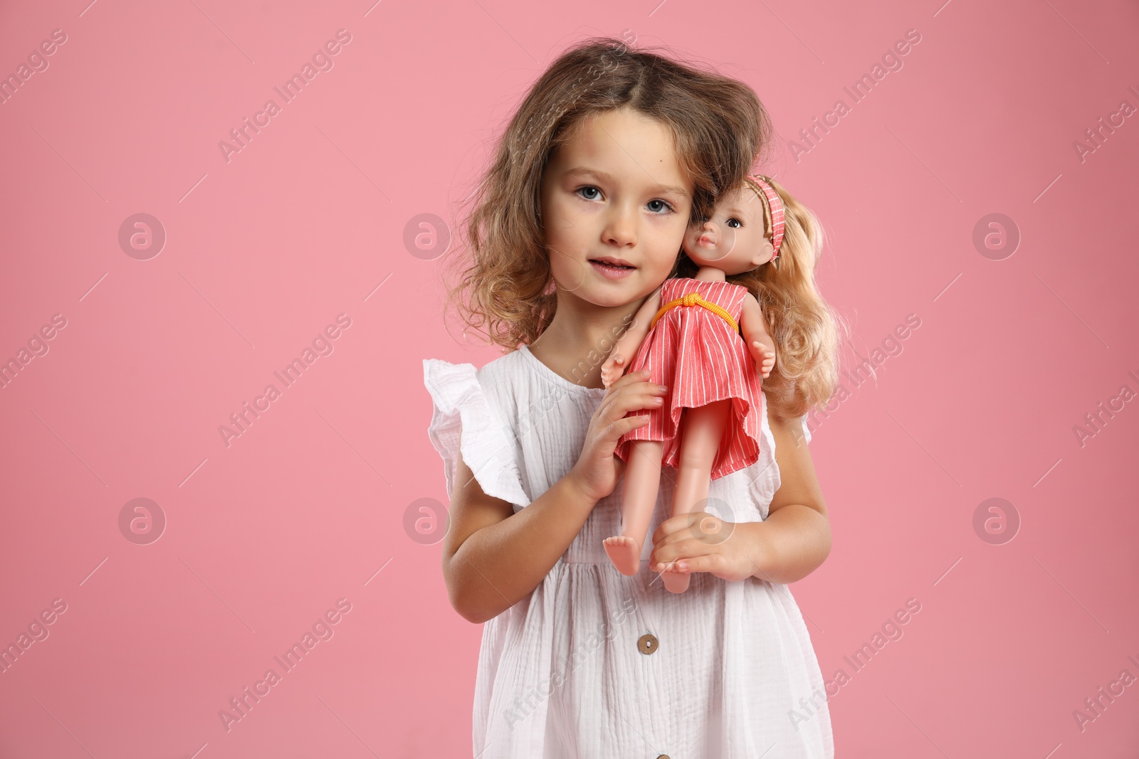 Photo of Cute little girl with doll on pink background