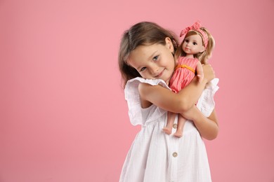 Photo of Cute little girl with doll on pink background. Space for text