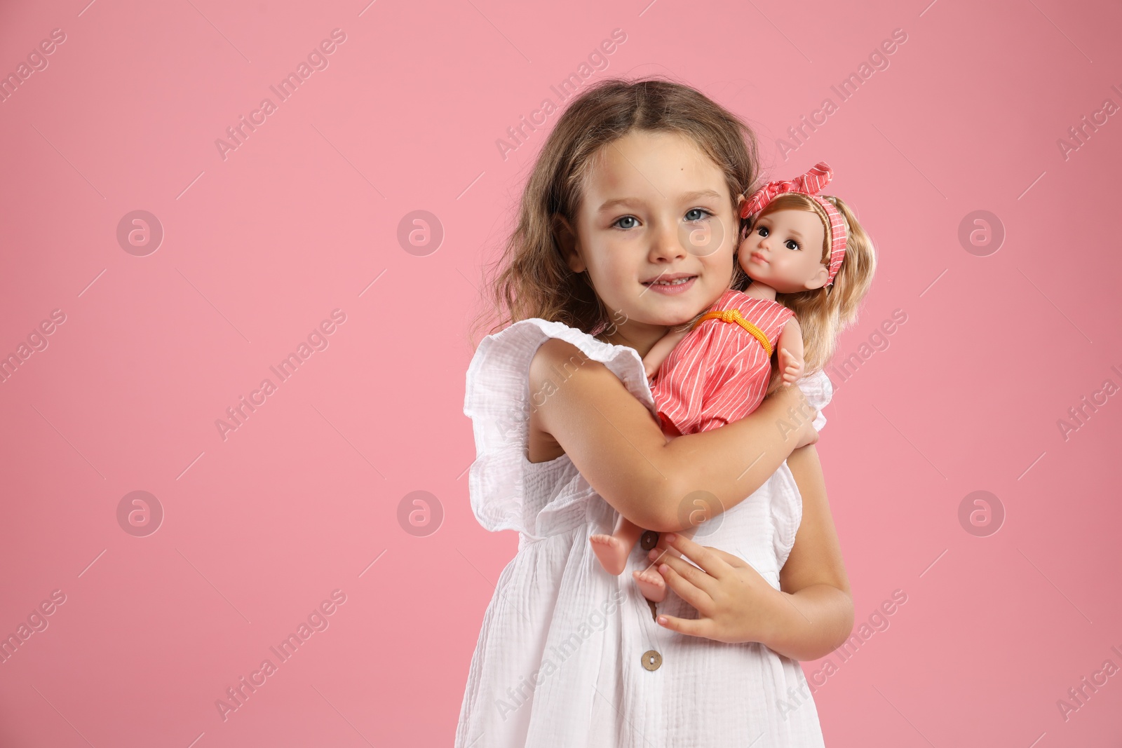 Photo of Cute little girl with doll on pink background. Space for text