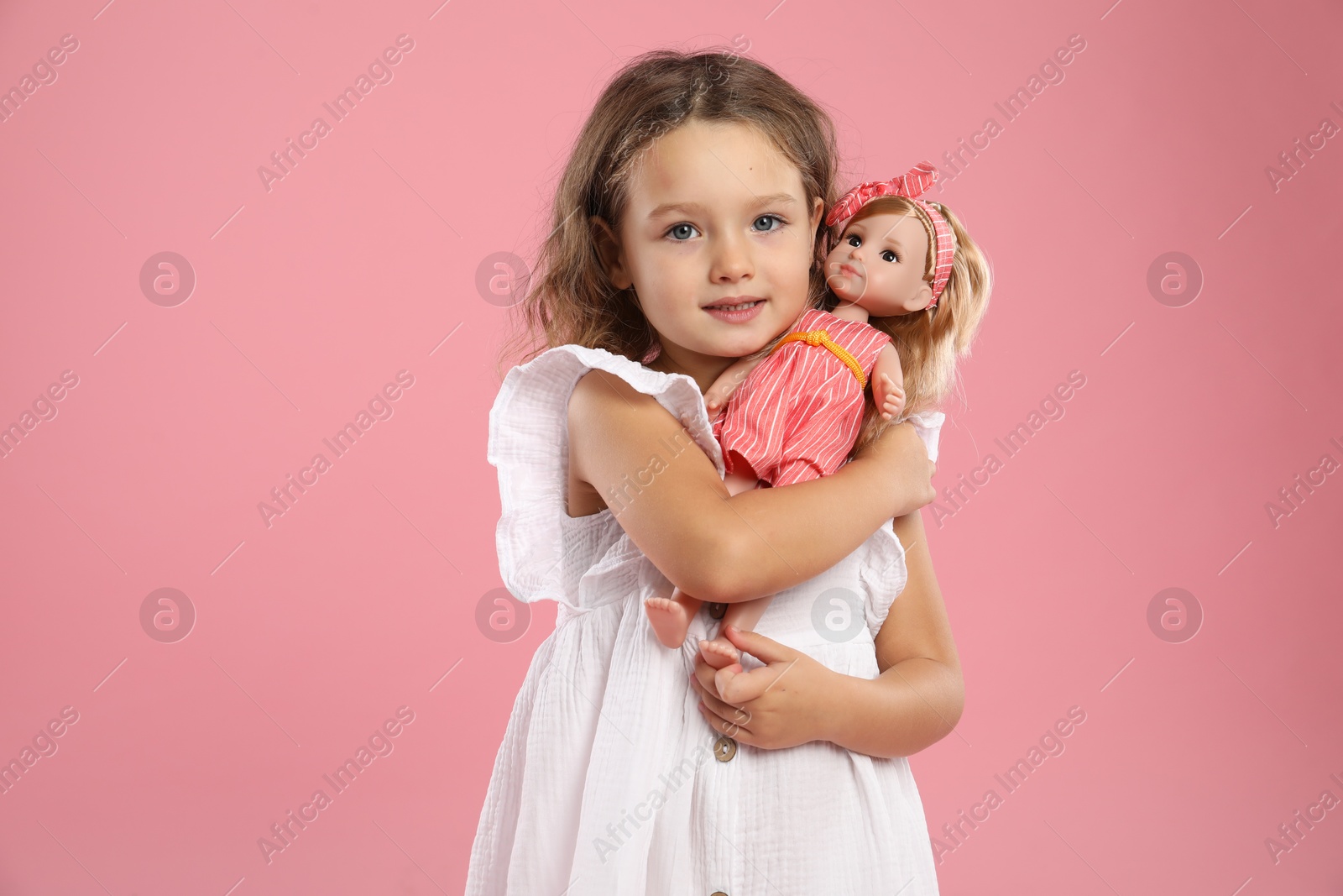 Photo of Cute little girl with doll on pink background