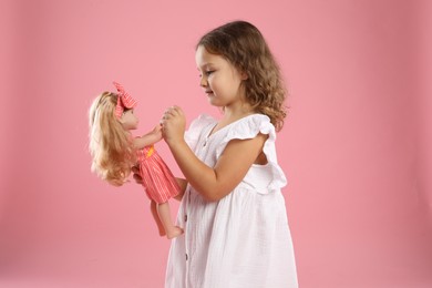 Photo of Cute little girl with doll on pink background