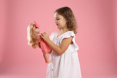 Photo of Cute little girl with doll on pink background