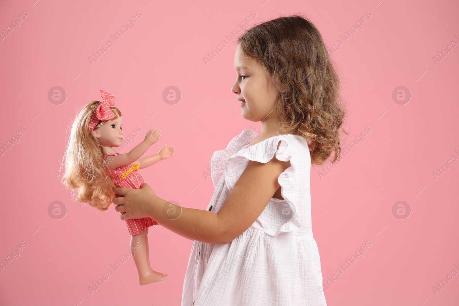 Photo of Cute little girl with doll on pink background