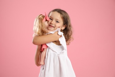 Photo of Cute little girl embracing her doll on pink background