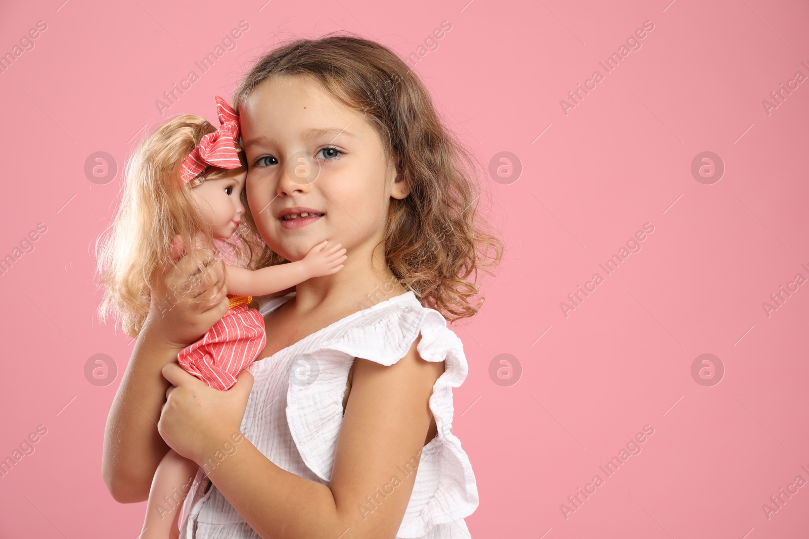 Photo of Cute little girl with doll on pink background. Space for text