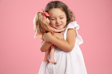 Photo of Cute little girl embracing her doll on pink background