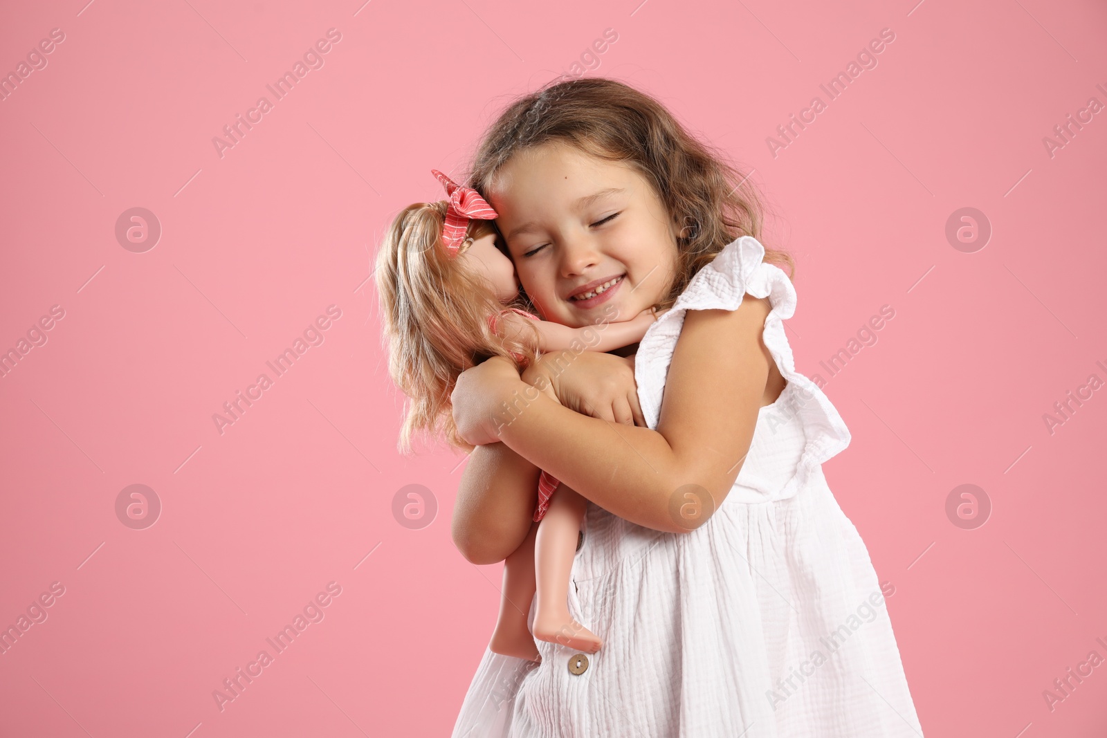 Photo of Cute little girl embracing her doll on pink background