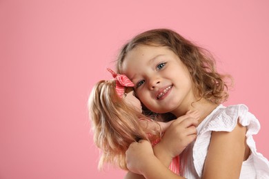 Photo of Cute little girl embracing her doll on pink background. Space for text