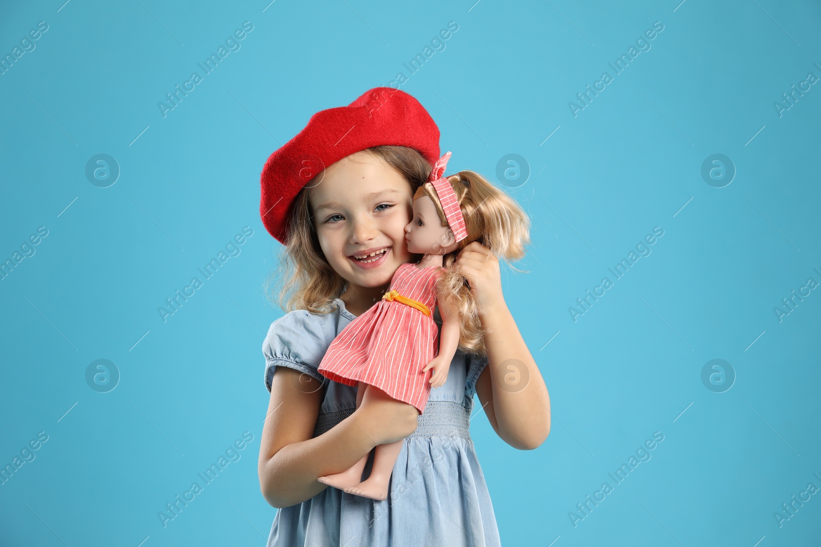 Photo of Cute little girl with doll on light blue background