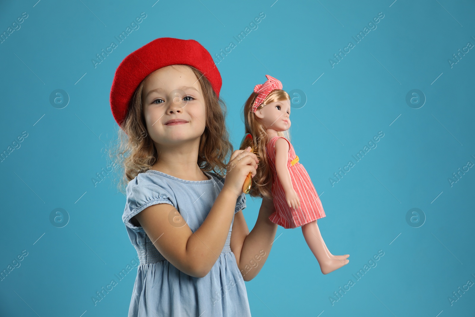 Photo of Cute little girl brushing doll's hair on light blue background