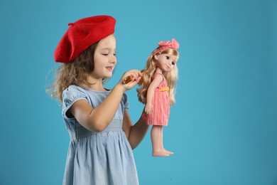 Photo of Cute little girl brushing doll's hair on light blue background. Space for text