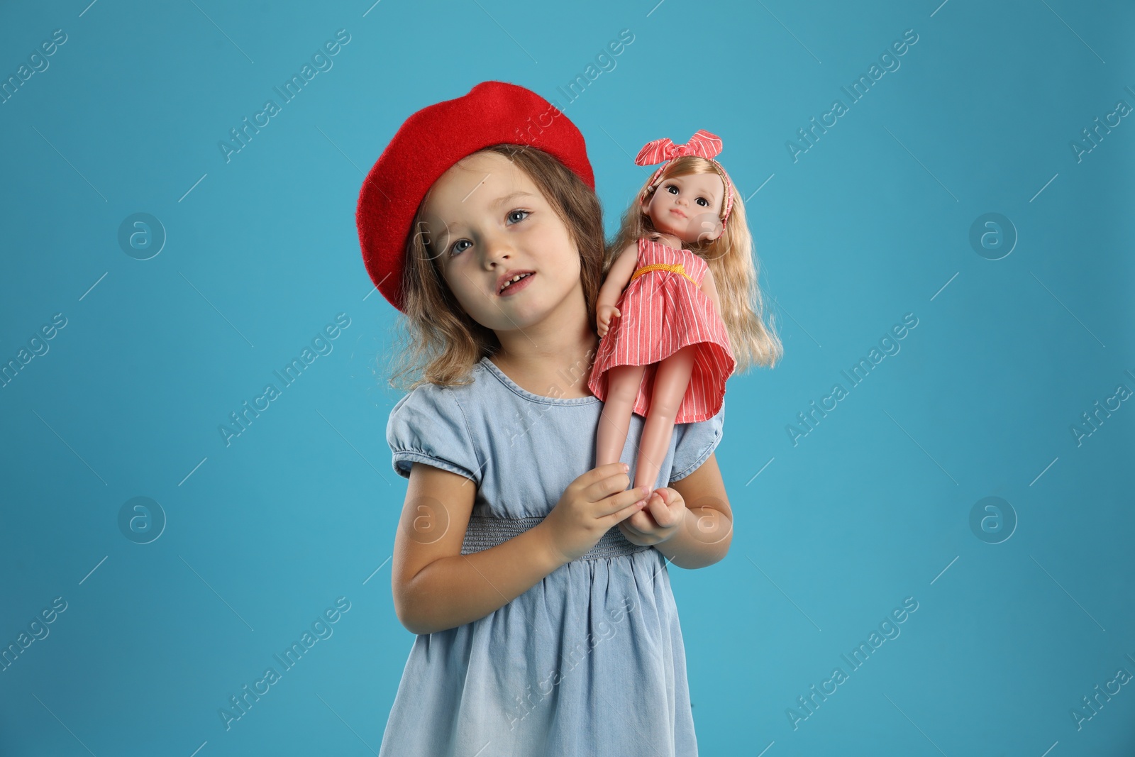 Photo of Cute little girl with doll on light blue background