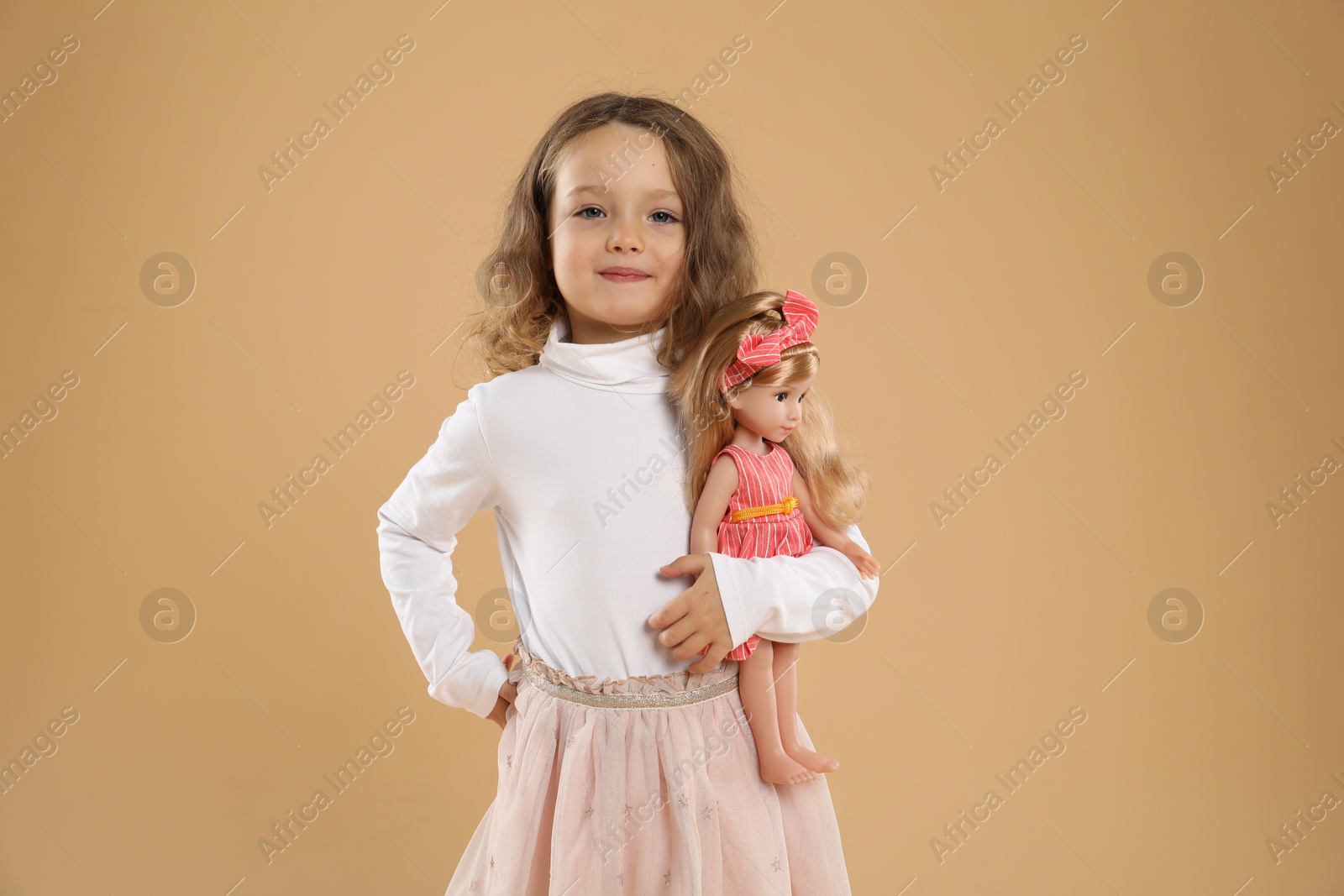 Photo of Cute little girl with doll on beige background