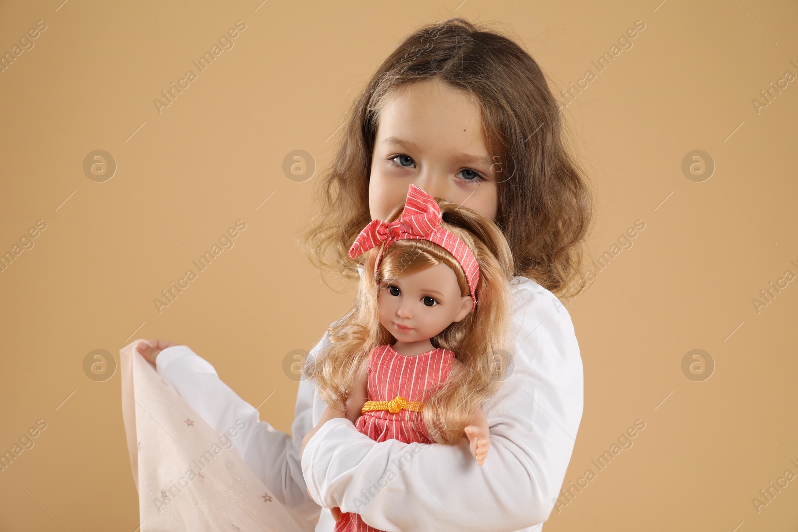 Photo of Cute little girl with doll on beige background