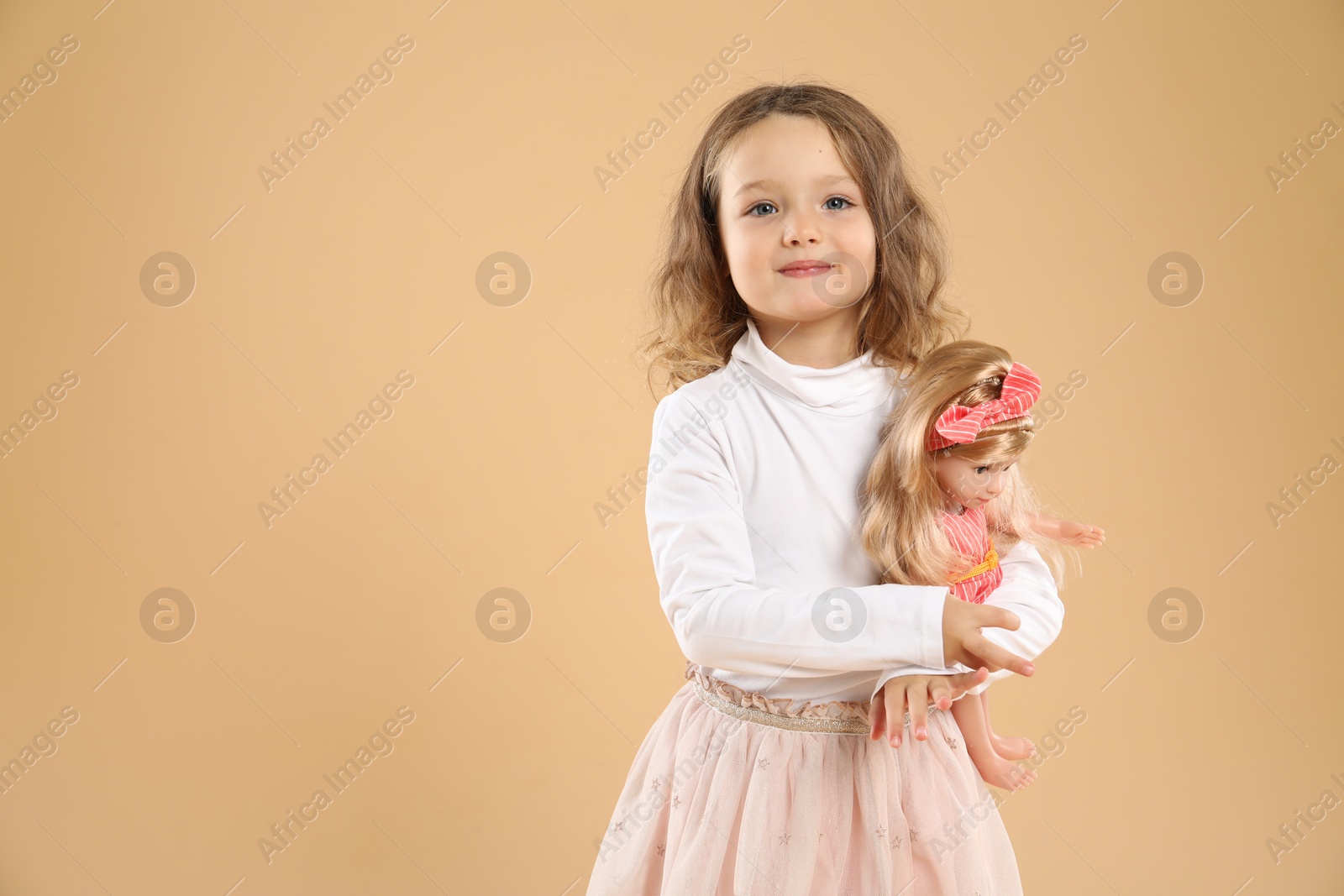 Photo of Cute little girl with doll on beige background. Space for text