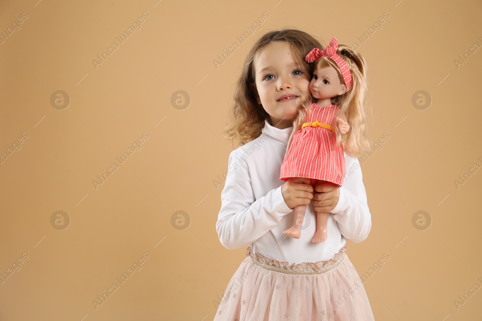 Photo of Cute little girl with doll on beige background. Space for text