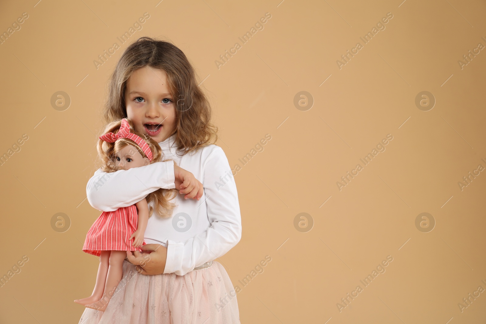 Photo of Cute little girl with doll on beige background. Space for text