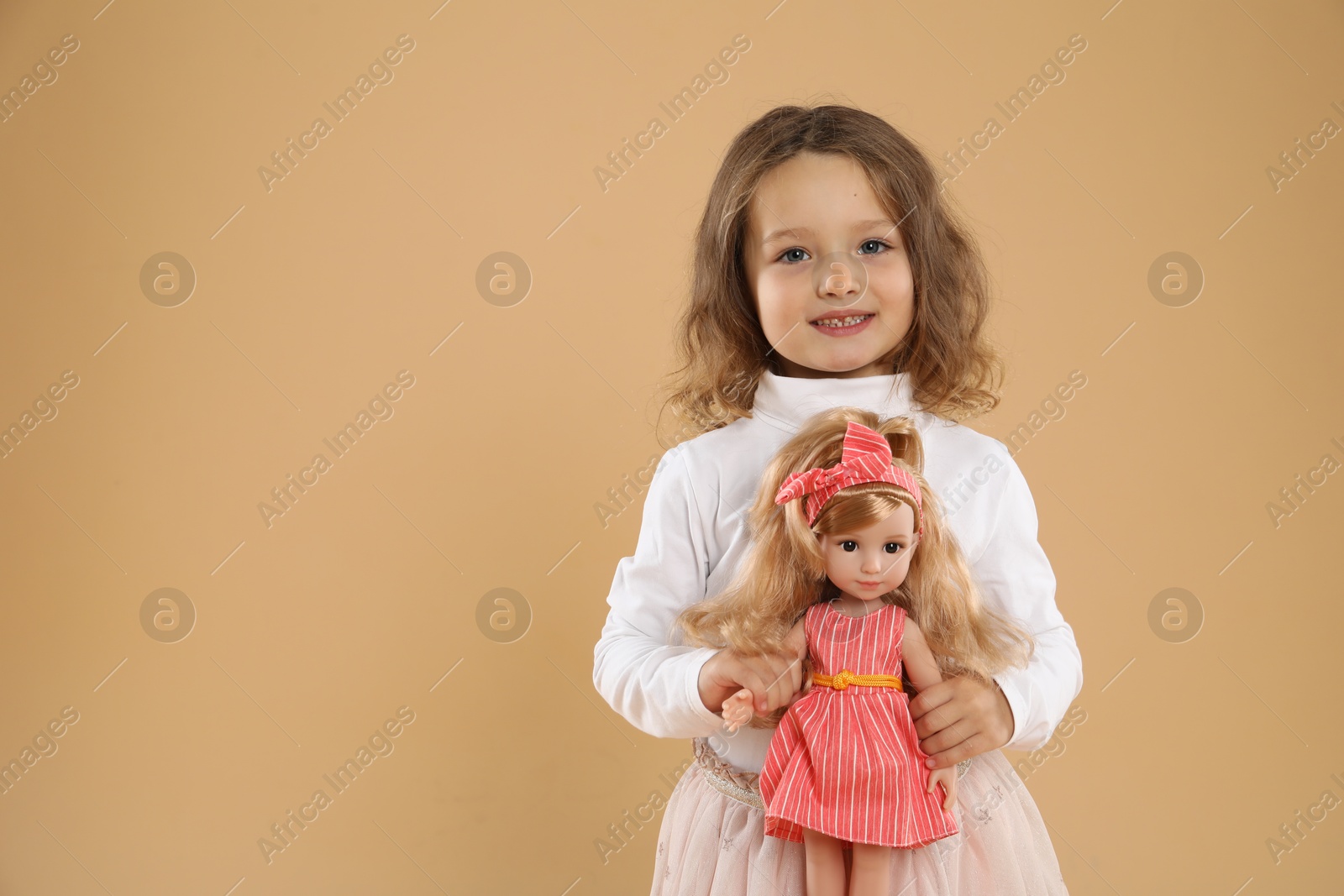 Photo of Cute little girl with doll on beige background. Space for text