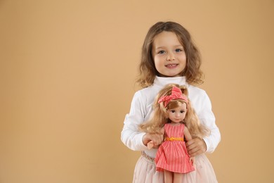 Photo of Cute little girl with doll on beige background. Space for text