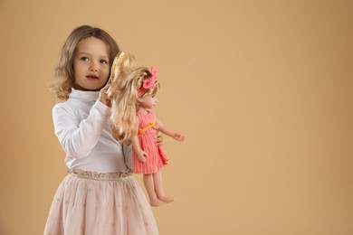 Photo of Cute little girl brushing doll's hair on beige background. Space for text