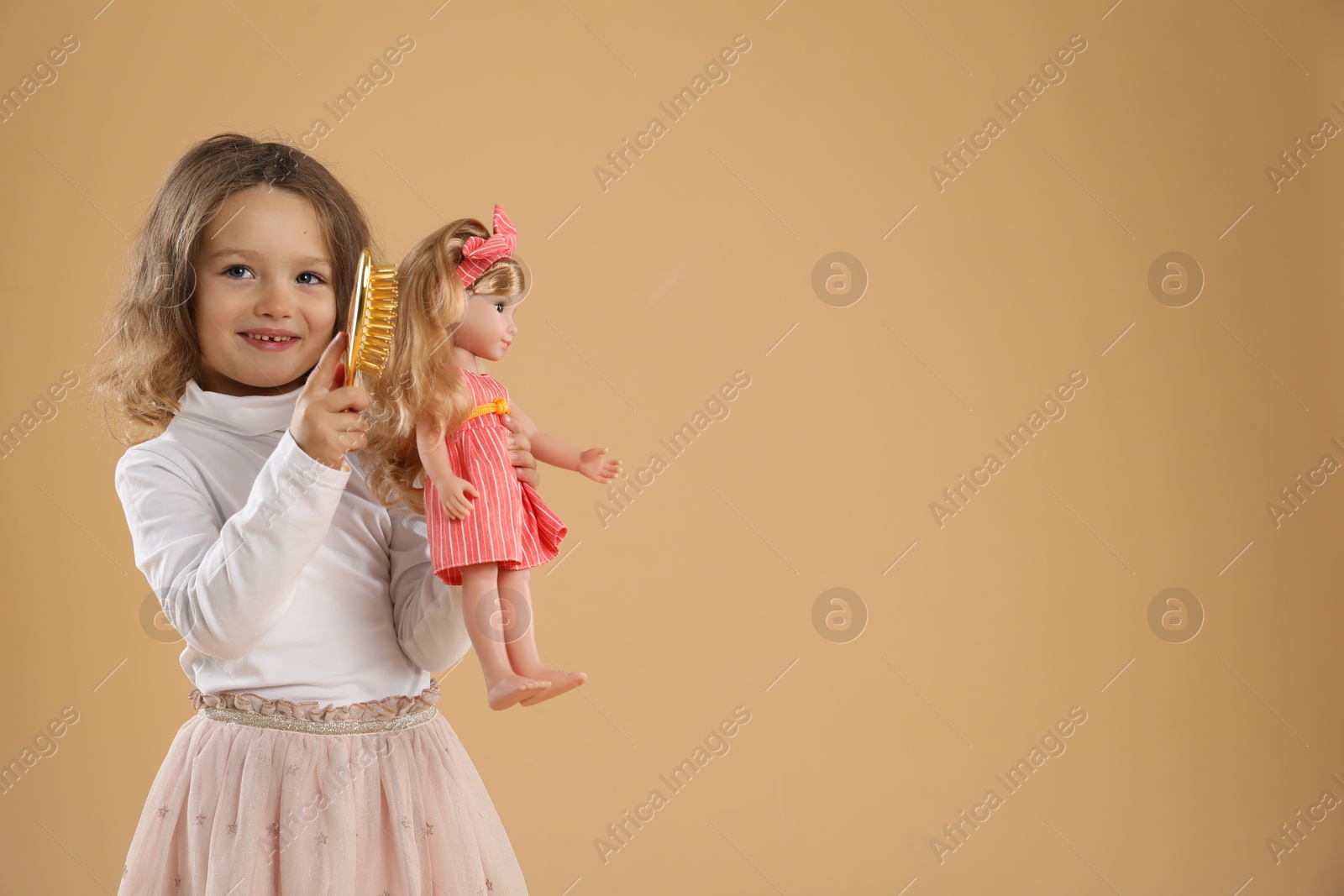 Photo of Cute little girl brushing doll's hair on beige background. Space for text