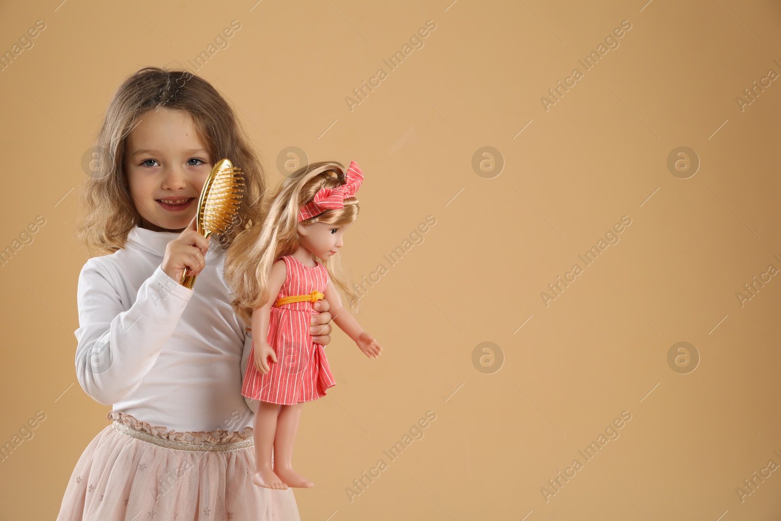 Photo of Cute little girl brushing doll's hair on beige background. Space for text