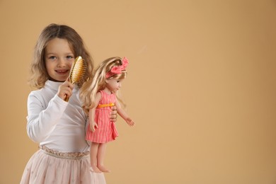 Photo of Cute little girl brushing doll's hair on beige background. Space for text