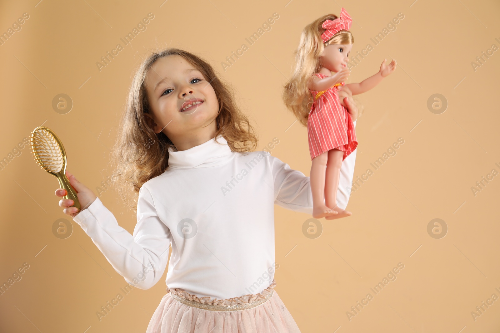 Photo of Cute little girl with doll and brush on beige background