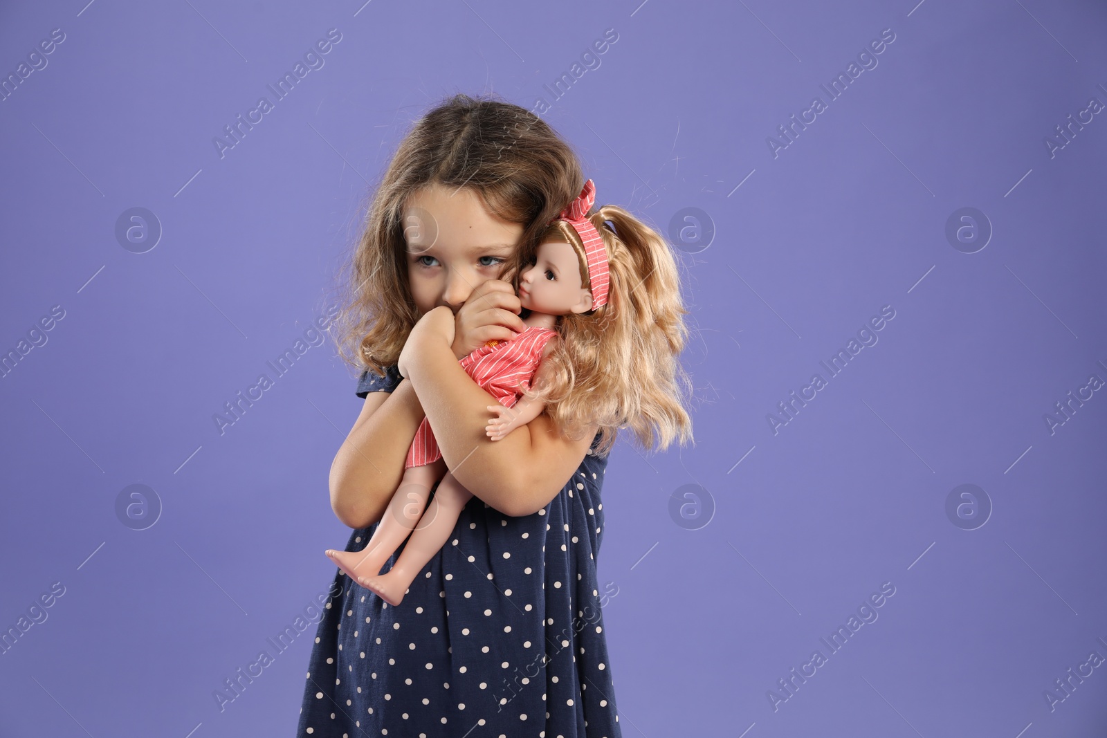 Photo of Cute little girl with doll on purple background