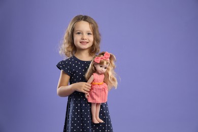 Photo of Cute little girl with doll on purple background. Space for text