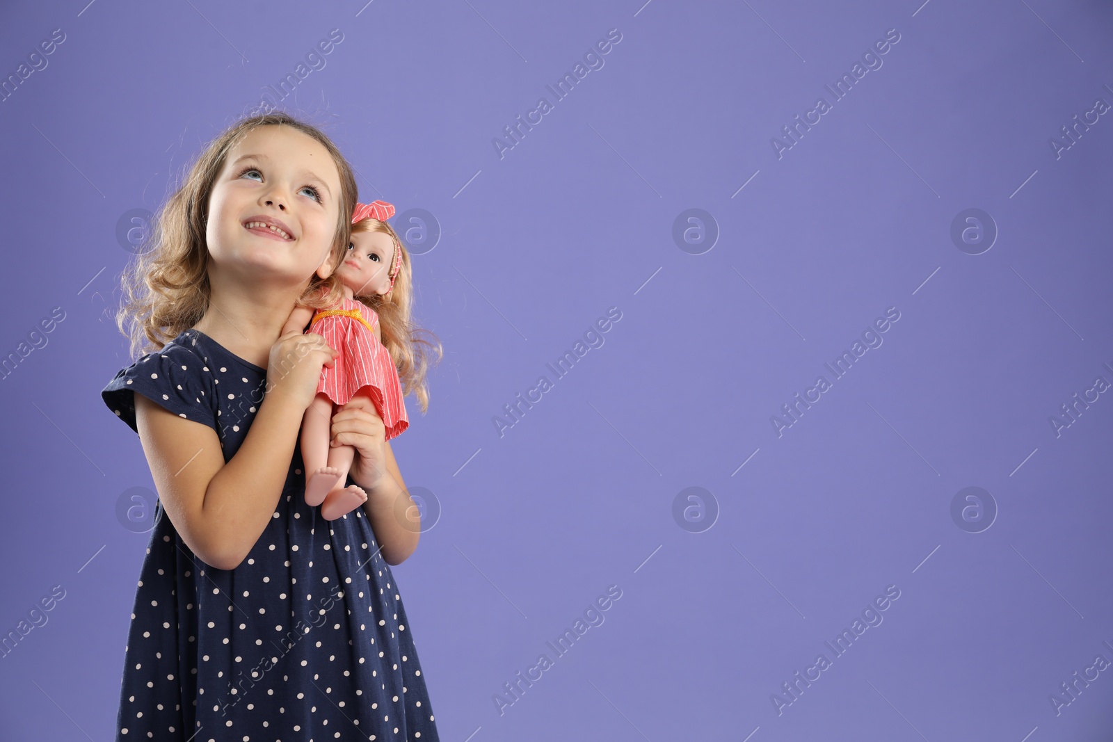 Photo of Cute little girl with doll on purple background. Space for text